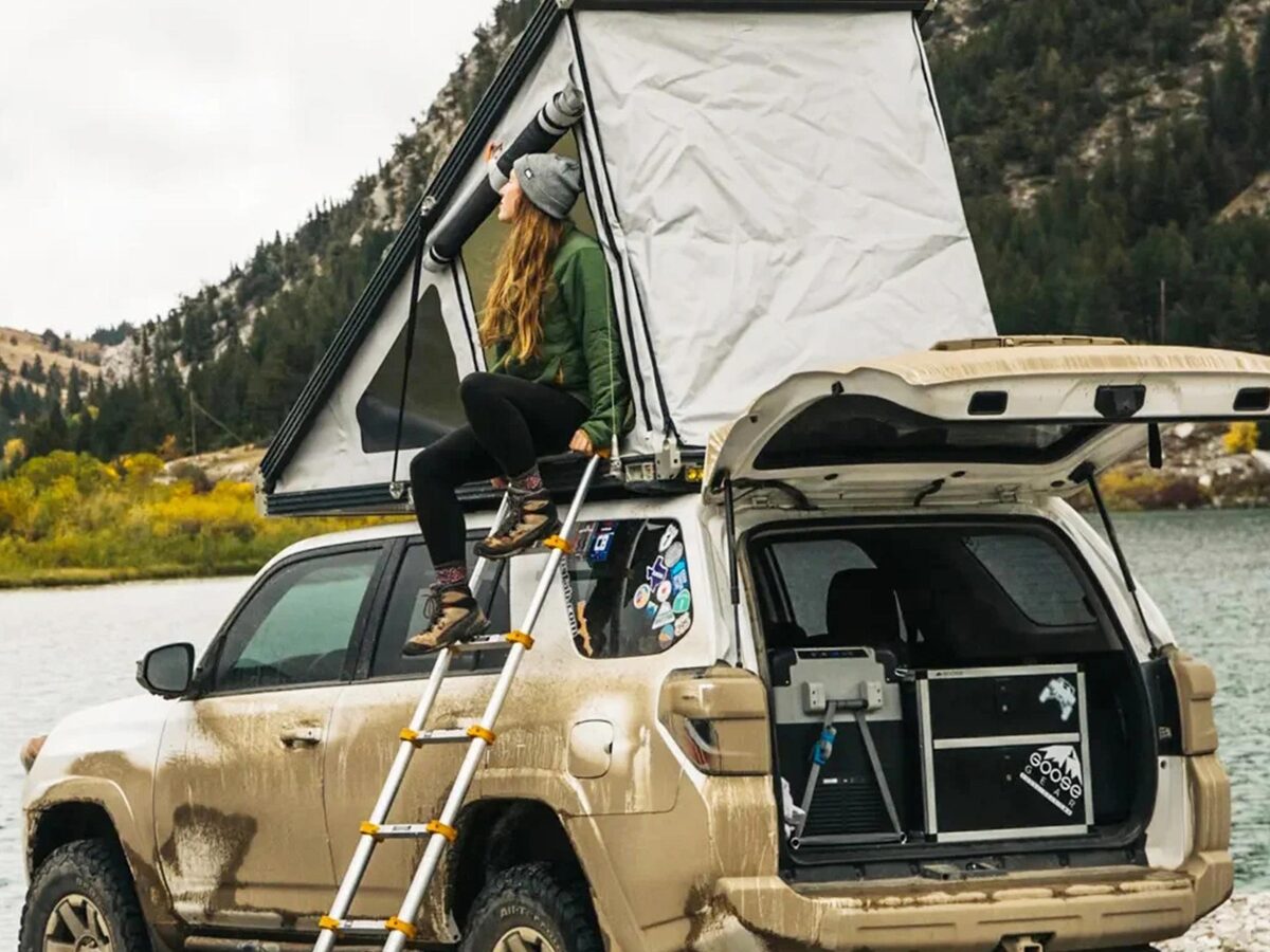 An overlanding SUV by a mountain lake with its rooftop tent and rear hatch held open by gas struts